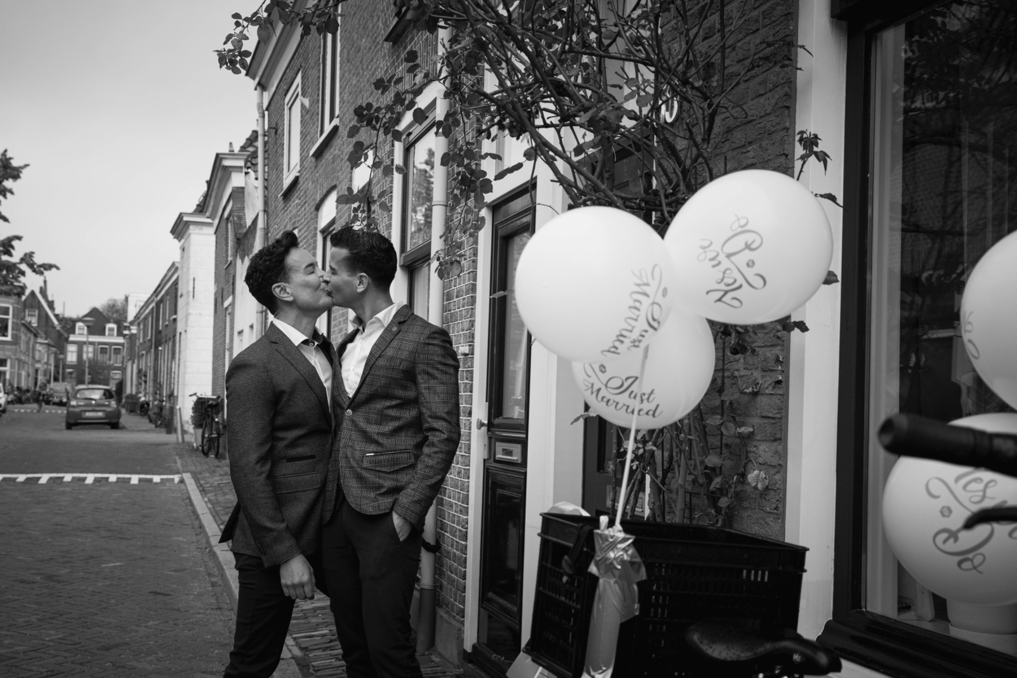 Een pasgetrouwd koppel kust elkaar in een straat met trouwballonnen